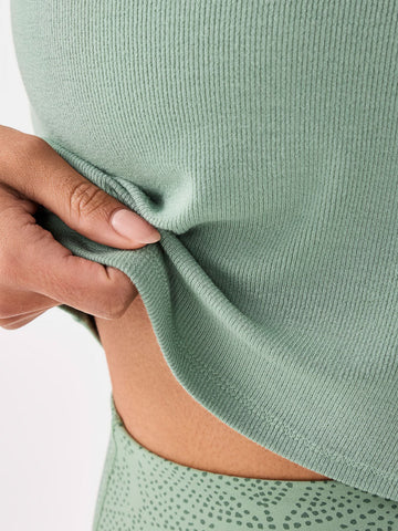 Close-up of a person wearing a green ribbed top with a plain background